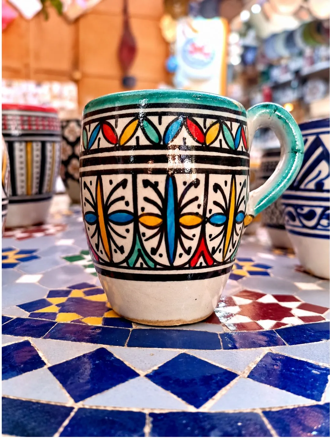 Turquoise hand-painted Moroccan ceramic mug with colorful traditional-inspired geometric decoration on mosaic tile.