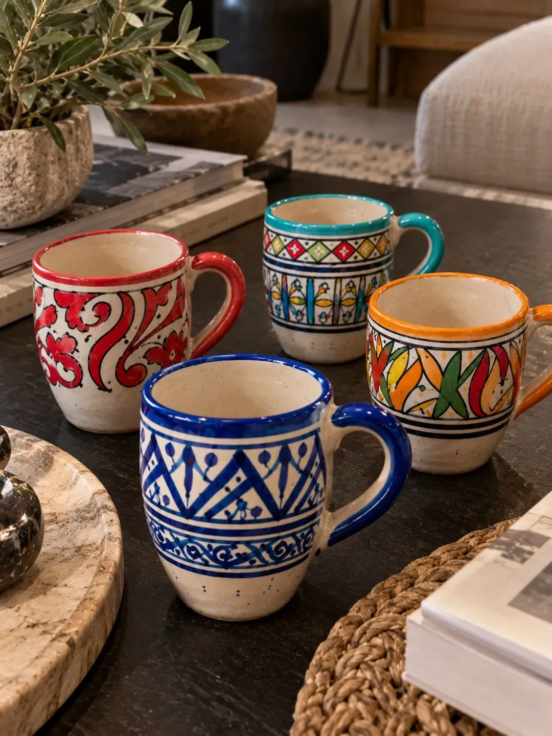 Four colorful hand-painted Moroccan ceramic mugs arranged on a contemporary coffee table.