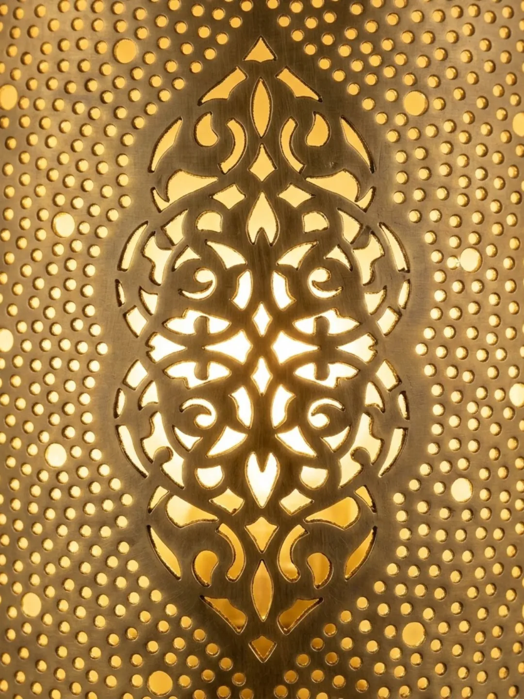 Close-up of the intricate ornamental cutout motif surrounded by small perforations on a brass Moroccan wall light.