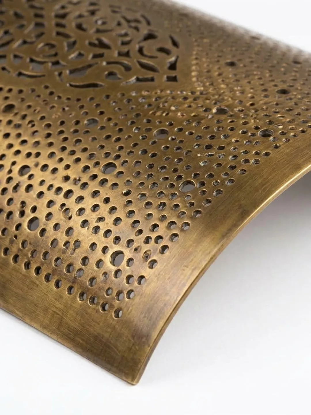 Close-up of the brass wall sconce showing rows of circular perforations, brushed metal texture, and warm antique-brass finish.