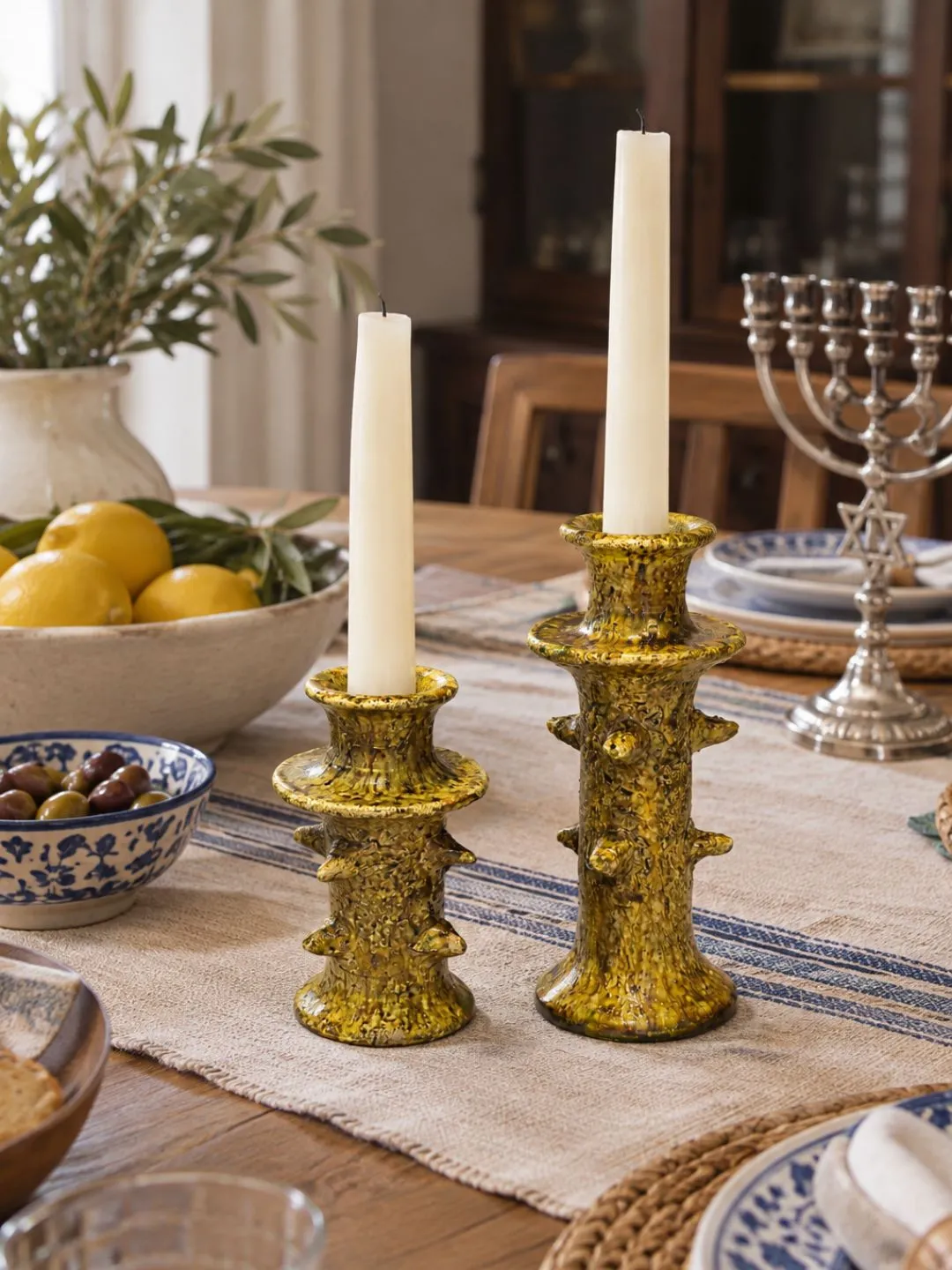 Pair of ochre-yellow ceramic taper candlesticks displayed with tableware and natural woven placemats