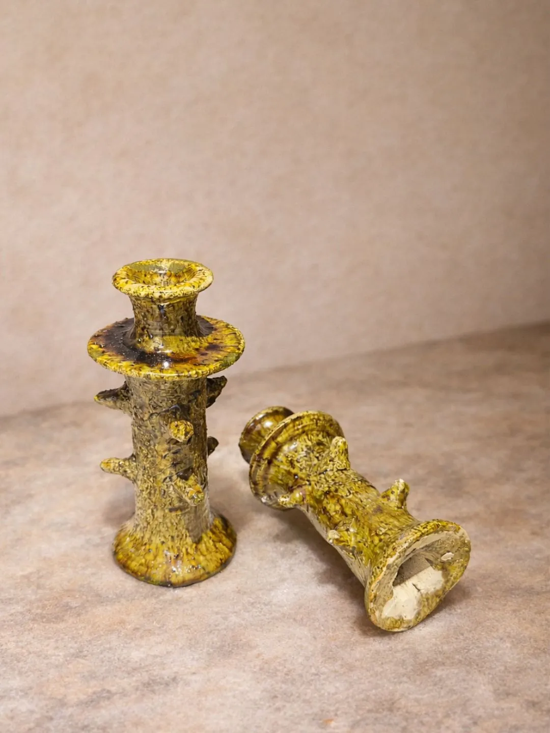 Two ochre-yellow ceramic candlesticks showing their sculptural shape and textured glaze from another angle