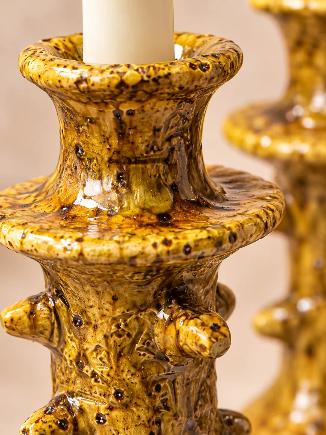 Macro close-up of an ochre-yellow Tamegroute ceramic taper candle holder showing its glossy, speckled glaze and handcrafted surface details.